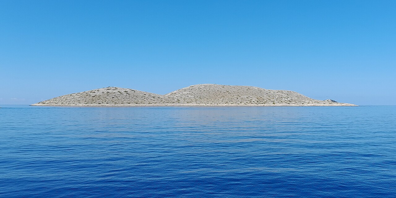 Falaises calcaires verticales spectaculaires de 80 mètres de Ravni Žakan dans le parc national de Kornati plongeant dans les eaux bleues profondes de l'Adriatique avec des entrées de grottes sous-marines et un yacht à la base